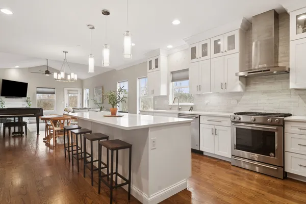 a kitchen with stainless steel appliances granite countertop a stove top oven a sink a dining table and chairs with wooden floor