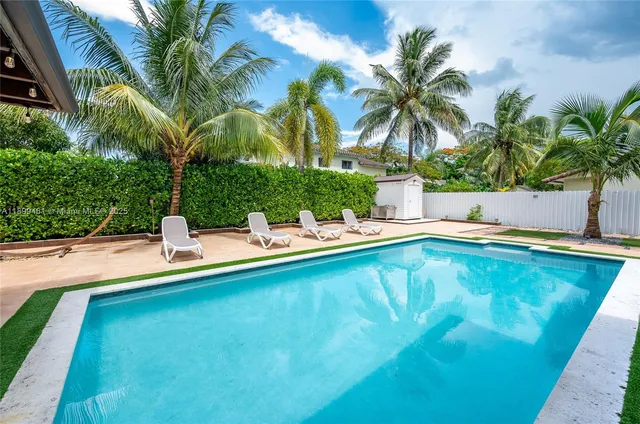 a view of a swimming pool with a lawn chairs under palm trees