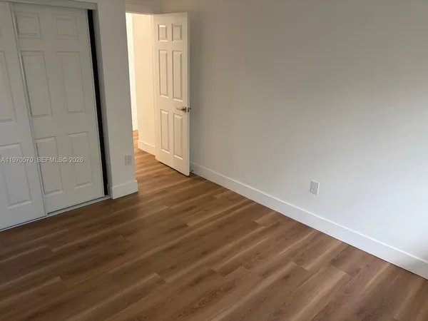 a view of an empty room with wooden floor and closet