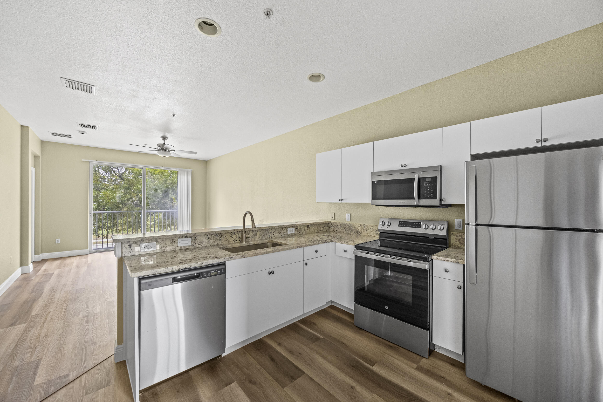 a kitchen with stainless steel appliances granite countertop white cabinets a sink a stove a refrigerator with grey cabinets and wooden floor