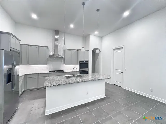 a large kitchen with granite countertop a stove a sink a refrigerator and white cabinets with wooden floor