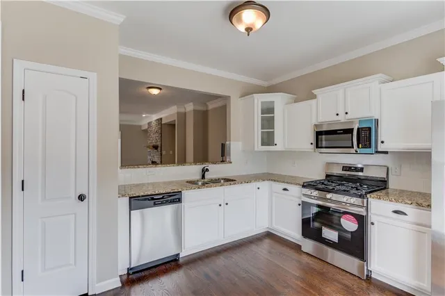 a kitchen with stainless steel appliances granite countertop a stove a sink and a white refrigerator with white cabinets