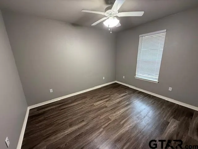 an empty room with wooden floor chandelier fan and windows