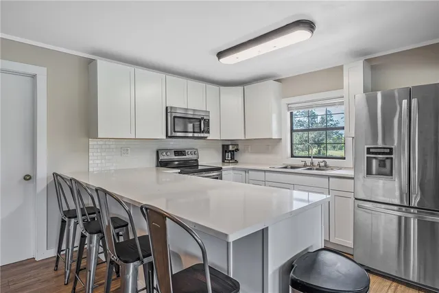 a kitchen with stainless steel appliances granite countertop a stove a refrigerator a microwave a sink dishwasher and white cabinets with wooden floor
