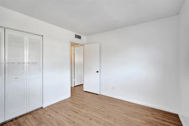 a view of an empty room with wooden floor and closet