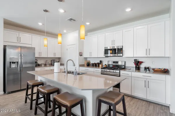 a kitchen with stainless steel appliances granite countertop white cabinets a sink a stove a kitchen island and chairs