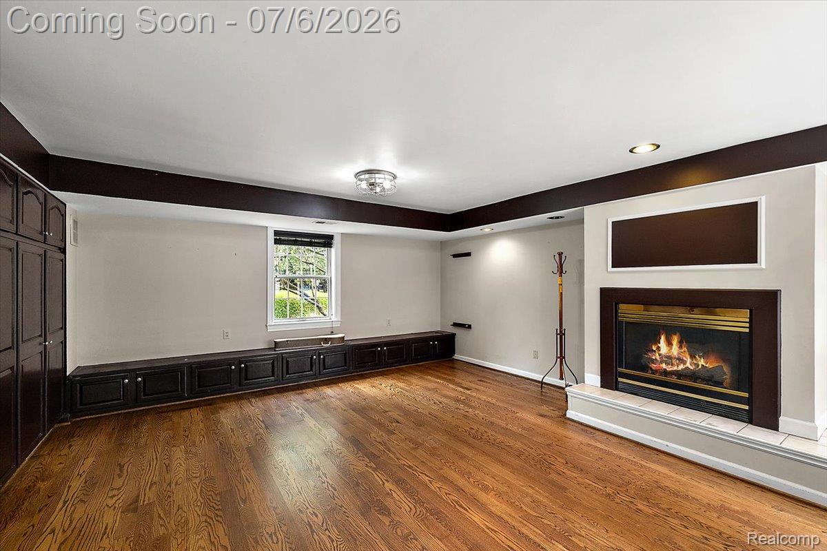 1051 Devonshire Road Grosse Pointe, MI 48230 - Photo 13 of 98 Spacious room featuring wood-finish flooring, an illuminated fireplace with a tile hearth, extensive built-in cabinetry, additional built-in storage benches, and a flush-mount ceiling light fixture