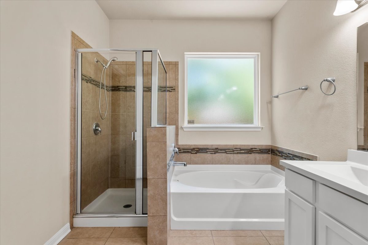 3451 Mayfield Ranch Boulevard, Unit 311 Round Rock, TX 78681 - Photo 22 of 40 Bathroom featuring a separate walk-in shower with glass enclosure, a built-in soaking tub, a single vanity with a white countertop, and a frosted window