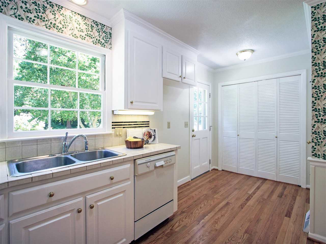 1324 Kingston Ridge Road Cary, NC 27511 - Photo 6 of 30 Kitchen has tile countertops and stainless steel sink. Built-in dishwasher. Louvered doors at the center of the photo are the laundry. Door shown at the left of the laundry leads to the backyard. Door to the right of the laundry leads to the garage. Kitchen