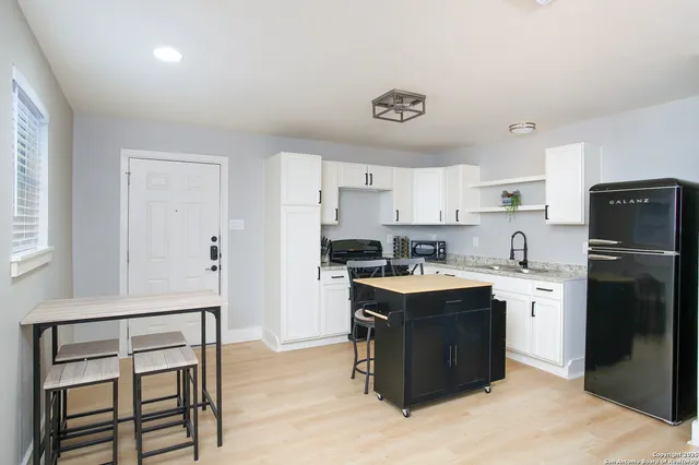 a kitchen with a refrigerator a stove a sink and white cabinets with wooden floor