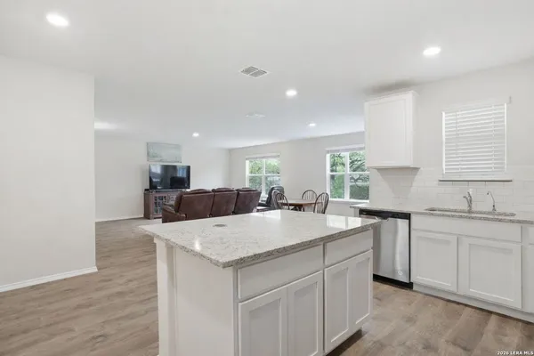 a large kitchen with granite countertop a sink and white cabinets with wooden floor