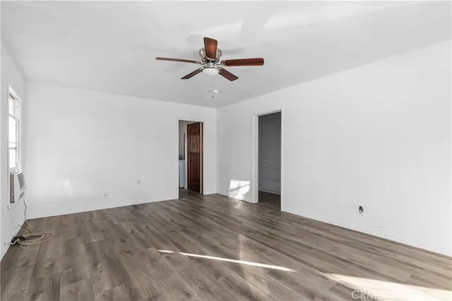 a view of an empty room with wooden floor and a ceiling fan