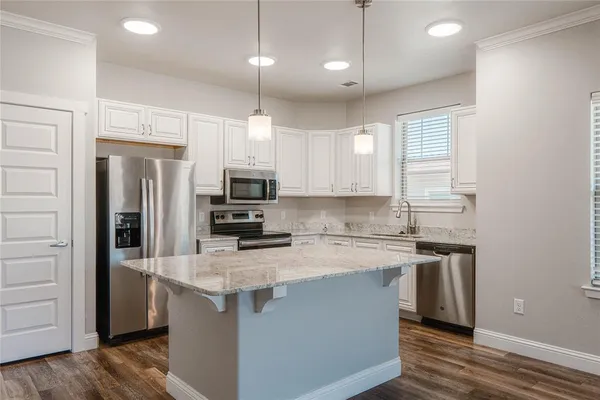 a kitchen with stainless steel appliances granite countertop a stove a refrigerator a sink and white cabinets with wooden floor