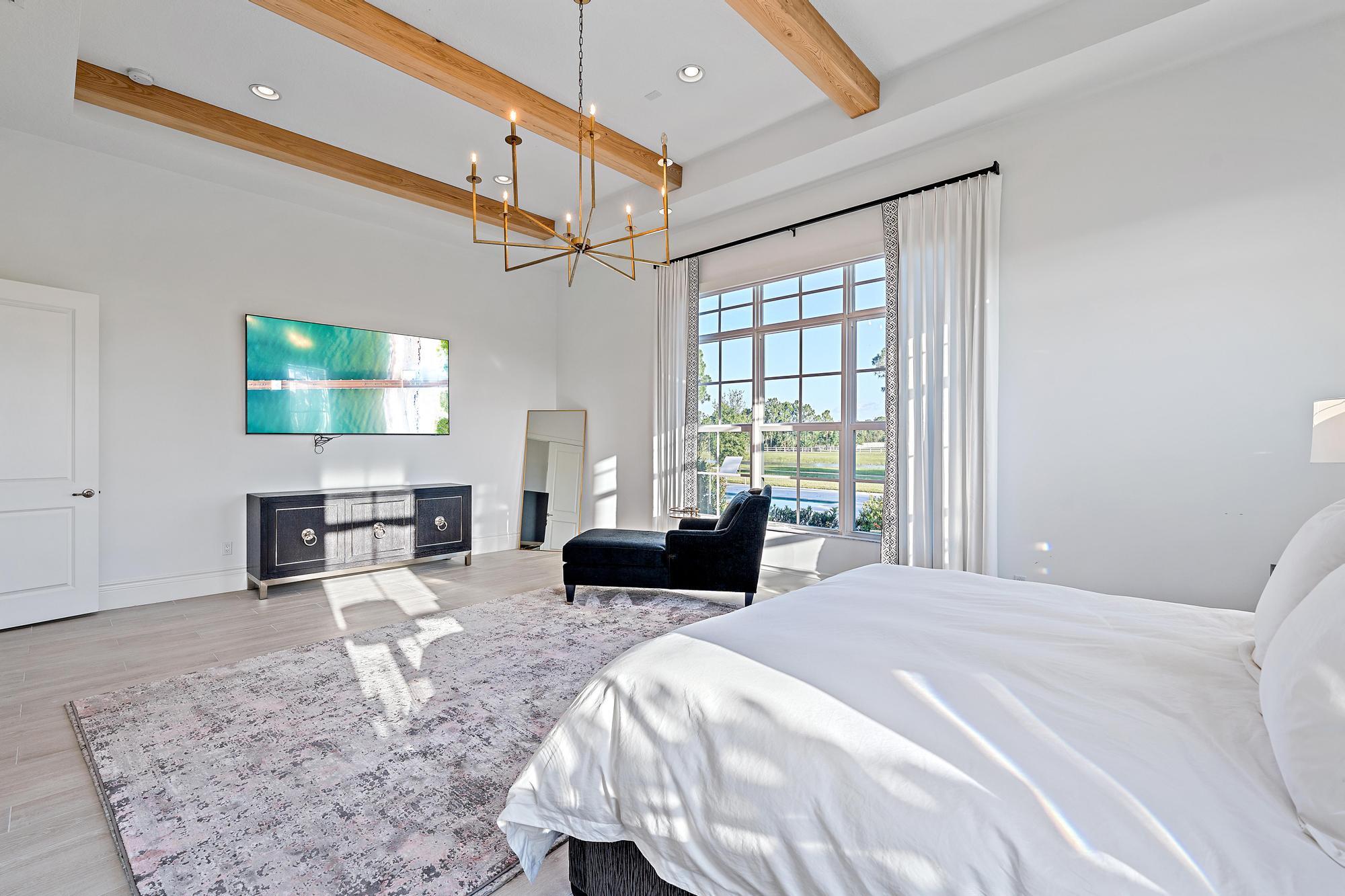 10096 Calabrese Trail Jupiter, FL 33478 - Photo 30 of 58 a bedroom with a bed a chandelier and flat screen tv