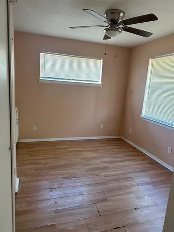 a view of a room with wooden floor a ceiling fan and windows