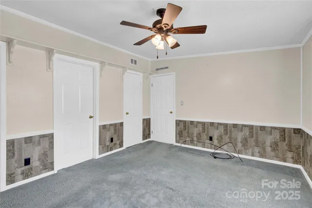 an empty room with chandelier fan and windows