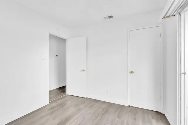 a view of an empty room with closet and wooden floor