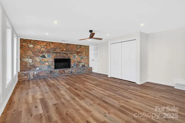 a view of an empty room with wooden floor fireplace and a window