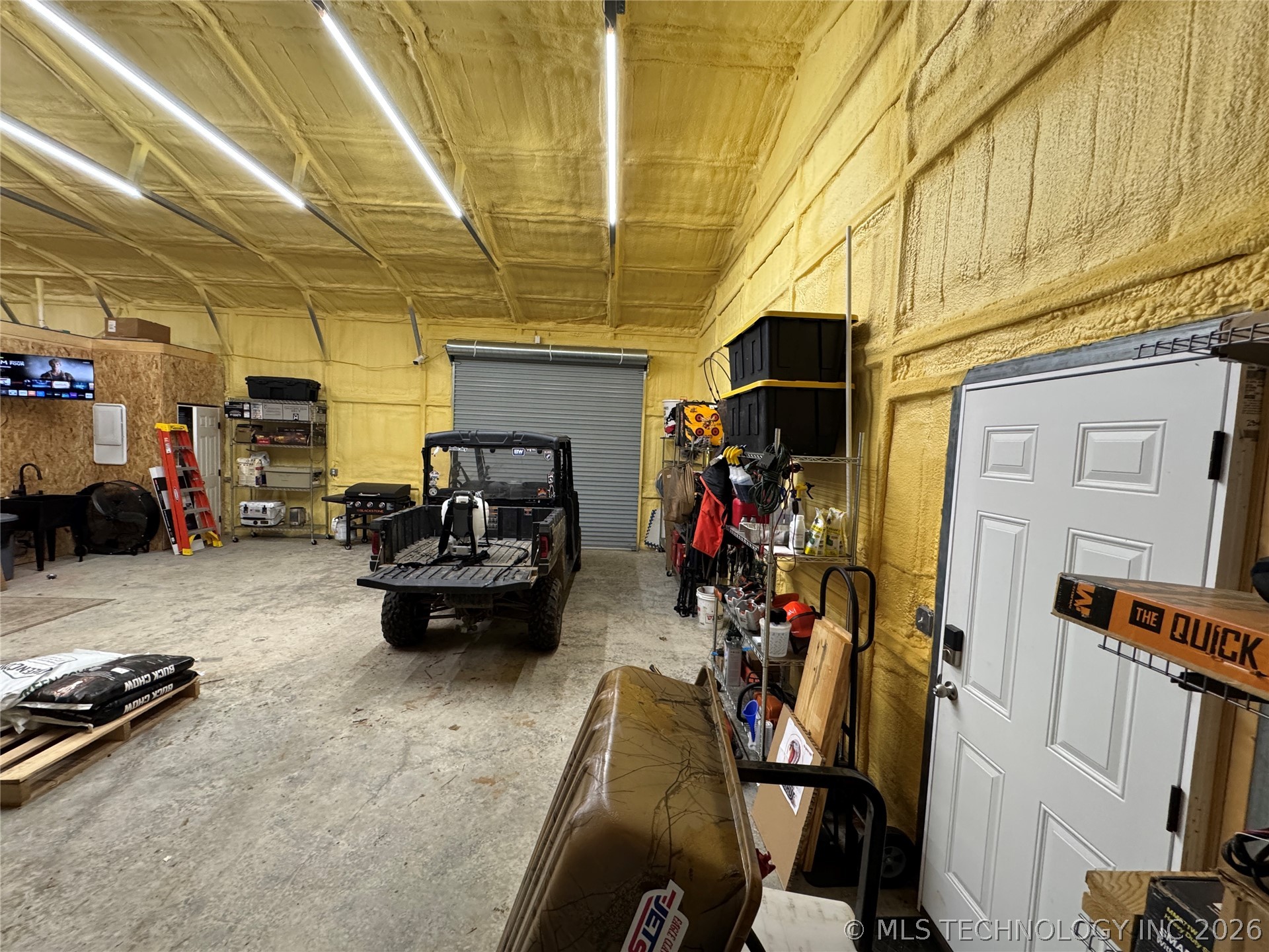 20862 East 1160th Road Keota, OK 74941 - Photo 35 of 47 Spacious garage interior featuring concrete flooring, a roll-up garage door, a paneled entry door, exposed wall studs, and ceiling-mounted linear lighting