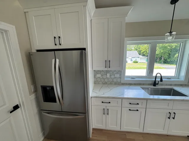 a kitchen with stainless steel appliances granite countertop a refrigerator sink and white cabinets with wooden floor