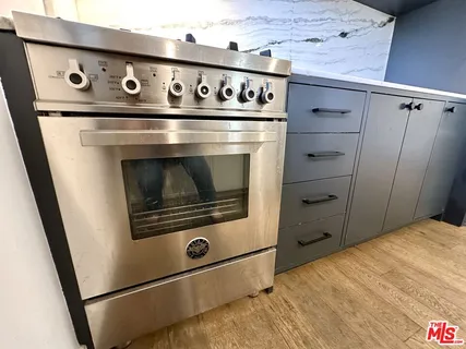 a stove top oven sitting inside of a kitchen with stainless steel appliances wooden floor