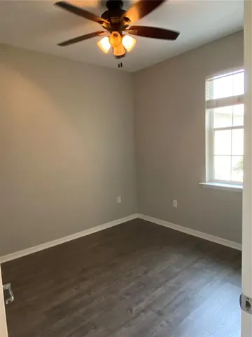 a view of an empty room with chandelier fan and wooden floor