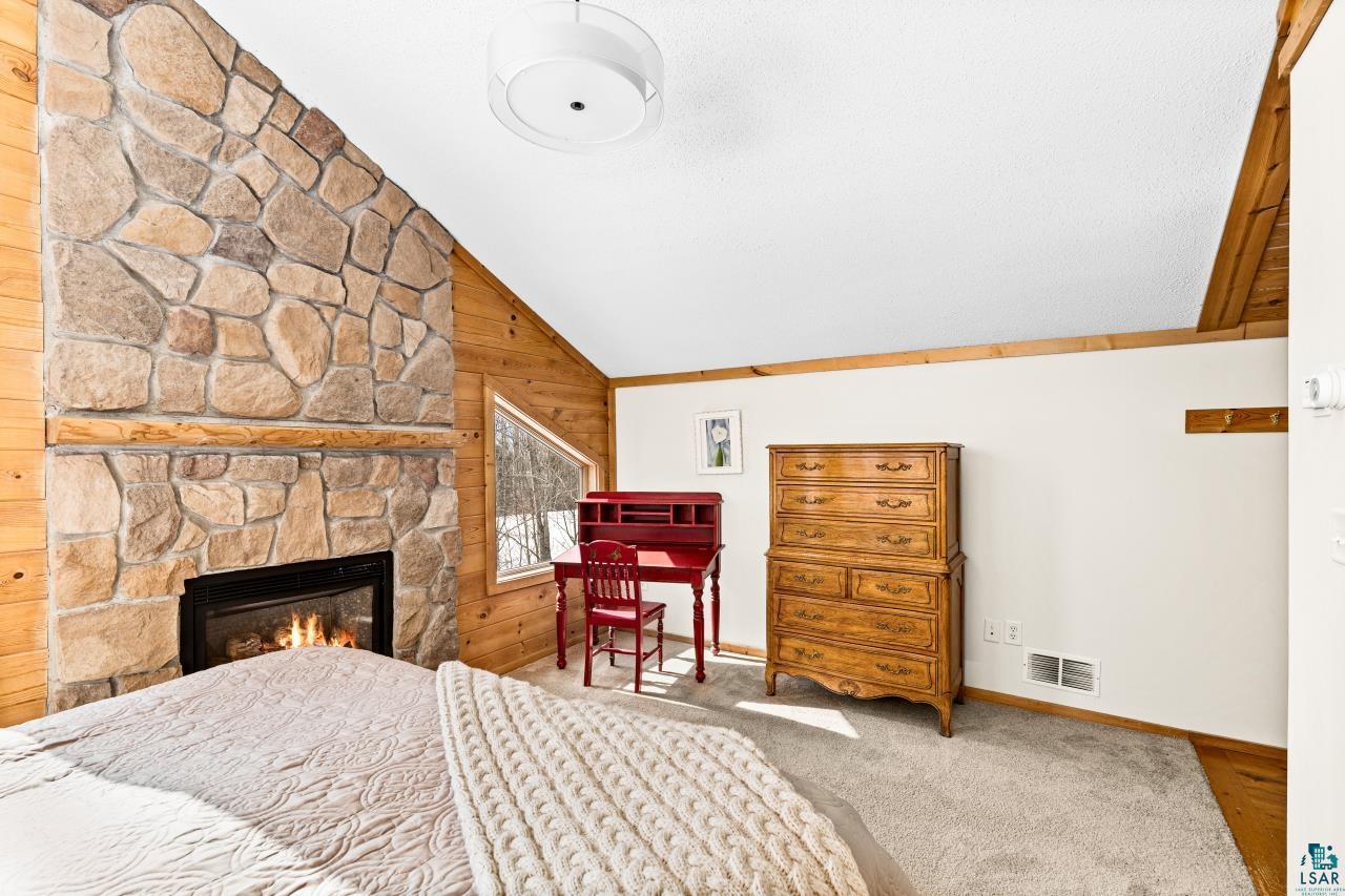 67 Snowshoe Trail Tofte, MN 55615 - Photo 8 of 42 Bedroom with lofted ceiling, wooden walls, light carpet, and a fireplace
