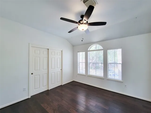 an empty room with wooden floor fan and windows