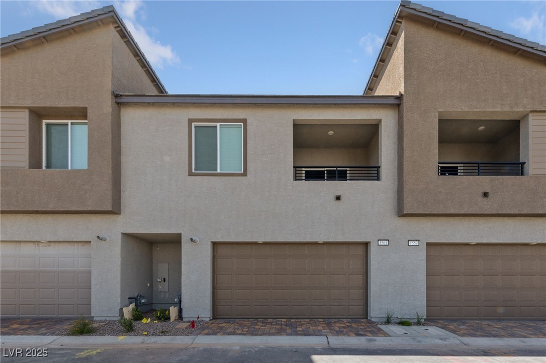 Back of house featuring a garage, stucco siding, and decorative driveway