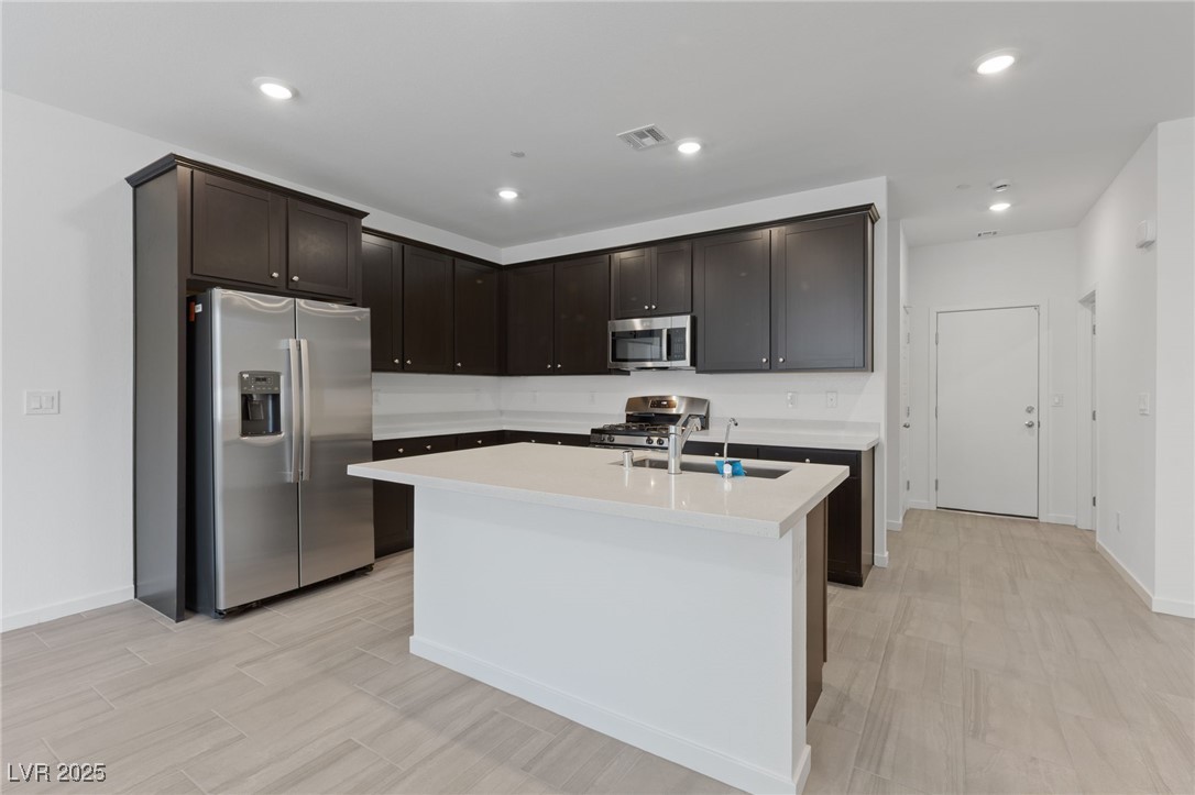 1561 Layla Crossing Avenue Henderson, NV 89002 - Photo 10 of 31 Kitchen with appliances with stainless steel finishes, recessed lighting, an island with sink, dark brown cabinetry, and light stone counters
