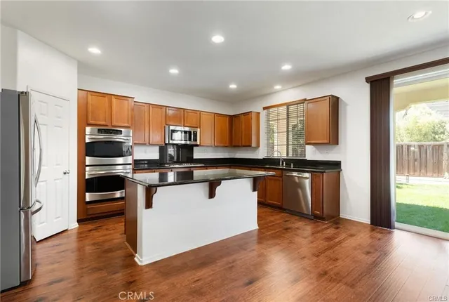 a kitchen with kitchen island granite countertop wooden floors stainless steel appliances a sink and a window