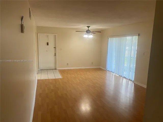 an empty room with wooden floor chandelier fan and windows