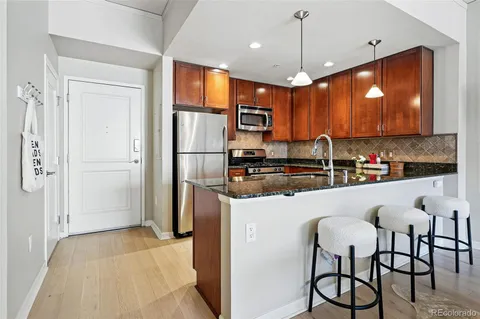 a kitchen with stainless steel appliances granite countertop a refrigerator a sink dishwasher a stove and a dining table with wooden floor