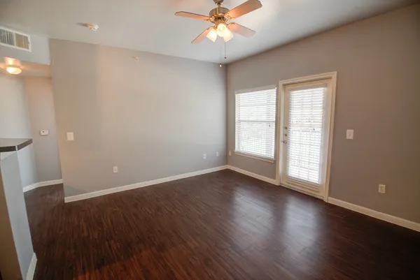 an empty room with wooden floor fan and windows