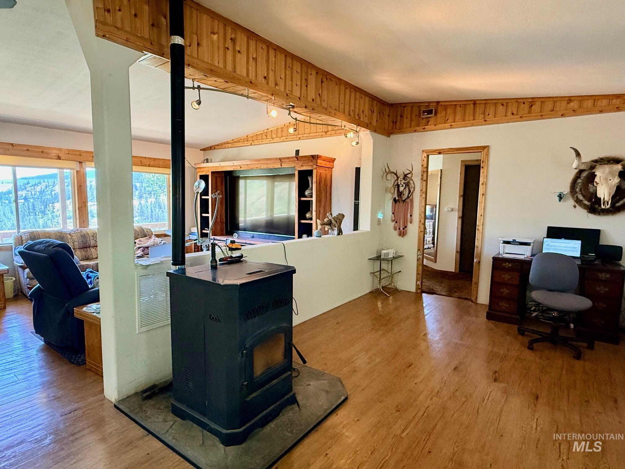 35322 River Road Lenore, ID 83541 - Photo 8 of 42 Spacious interior featuring wood-finish flooring, a freestanding black stove with a stone-finish base, and white walls with wood paneling accents