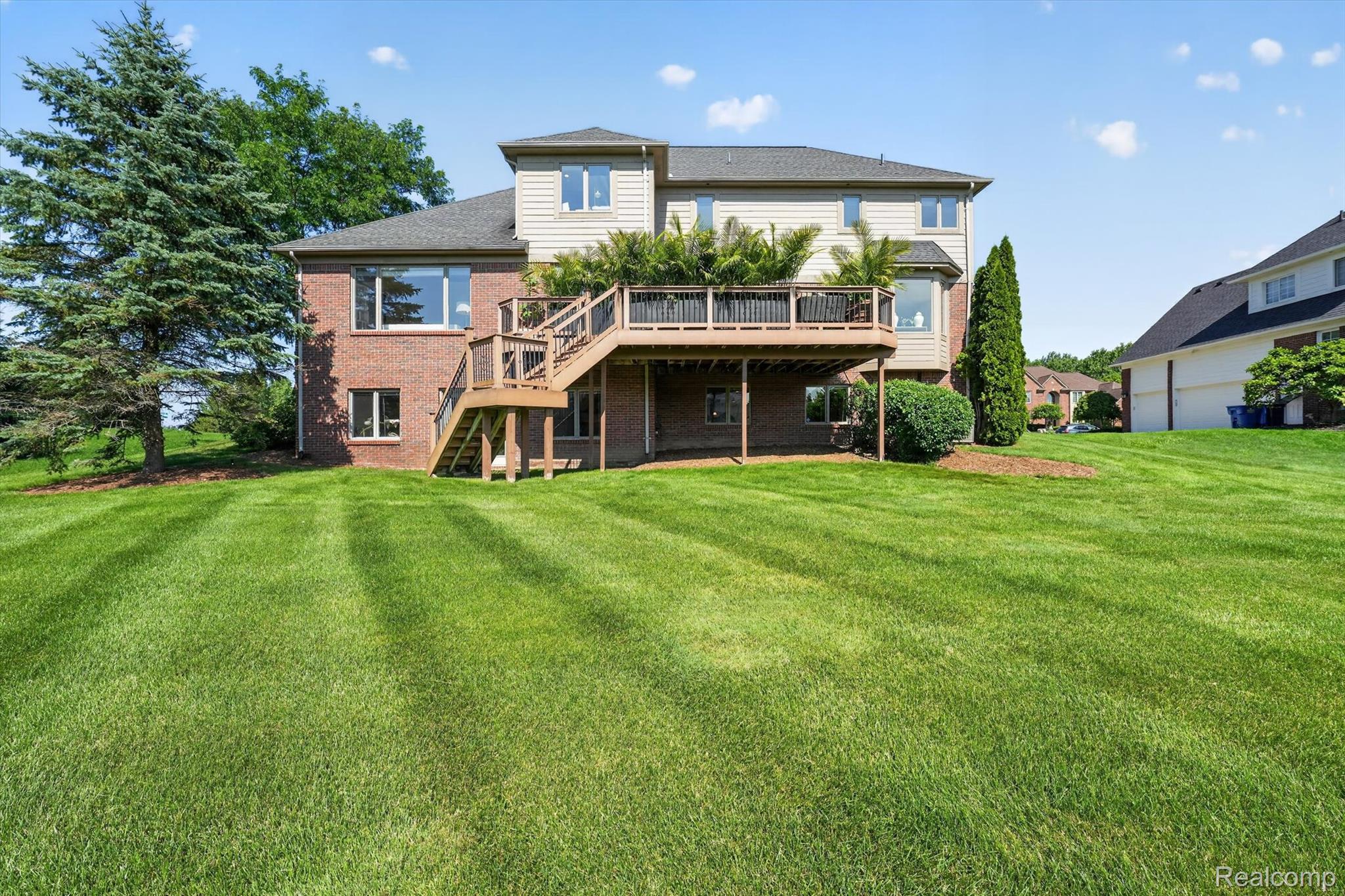 3804 Elk Drive Rochester, MI 48306 - Photo 57 of 75 Expansive rear yard featuring a multi-level deck with wood railings, a brick and siding exterior, multiple windows, and mature landscaping