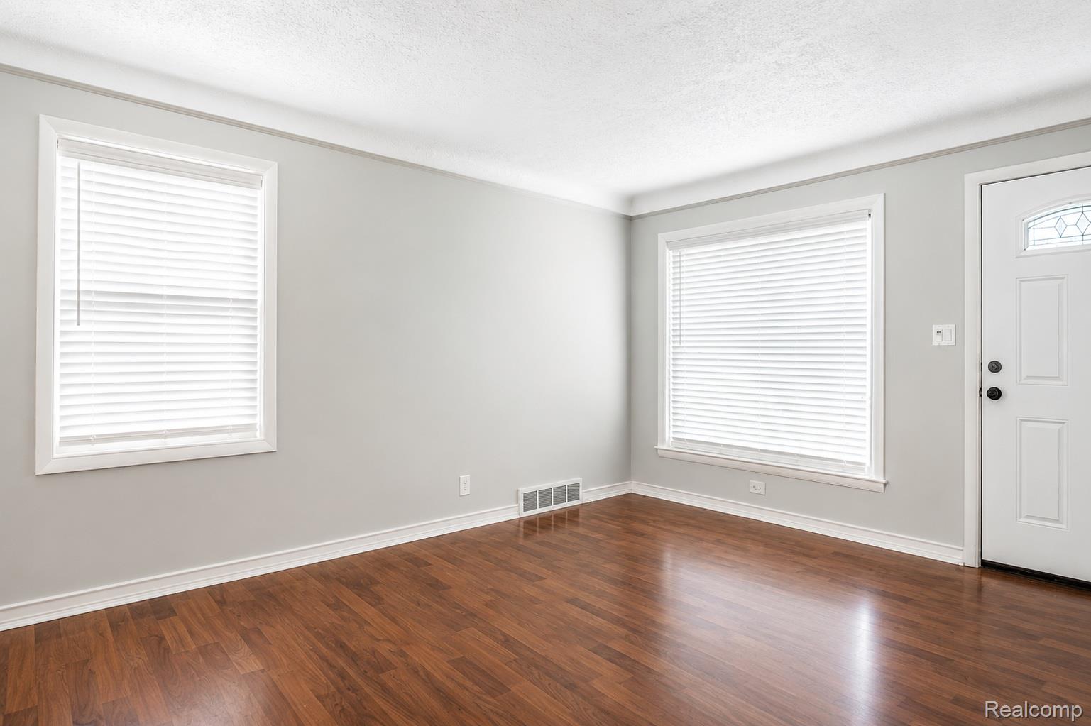 Bright, light-filled living space featuring expansive windows with plantation shutters, gleaming wood-finish flooring, and neutral wall finishes
