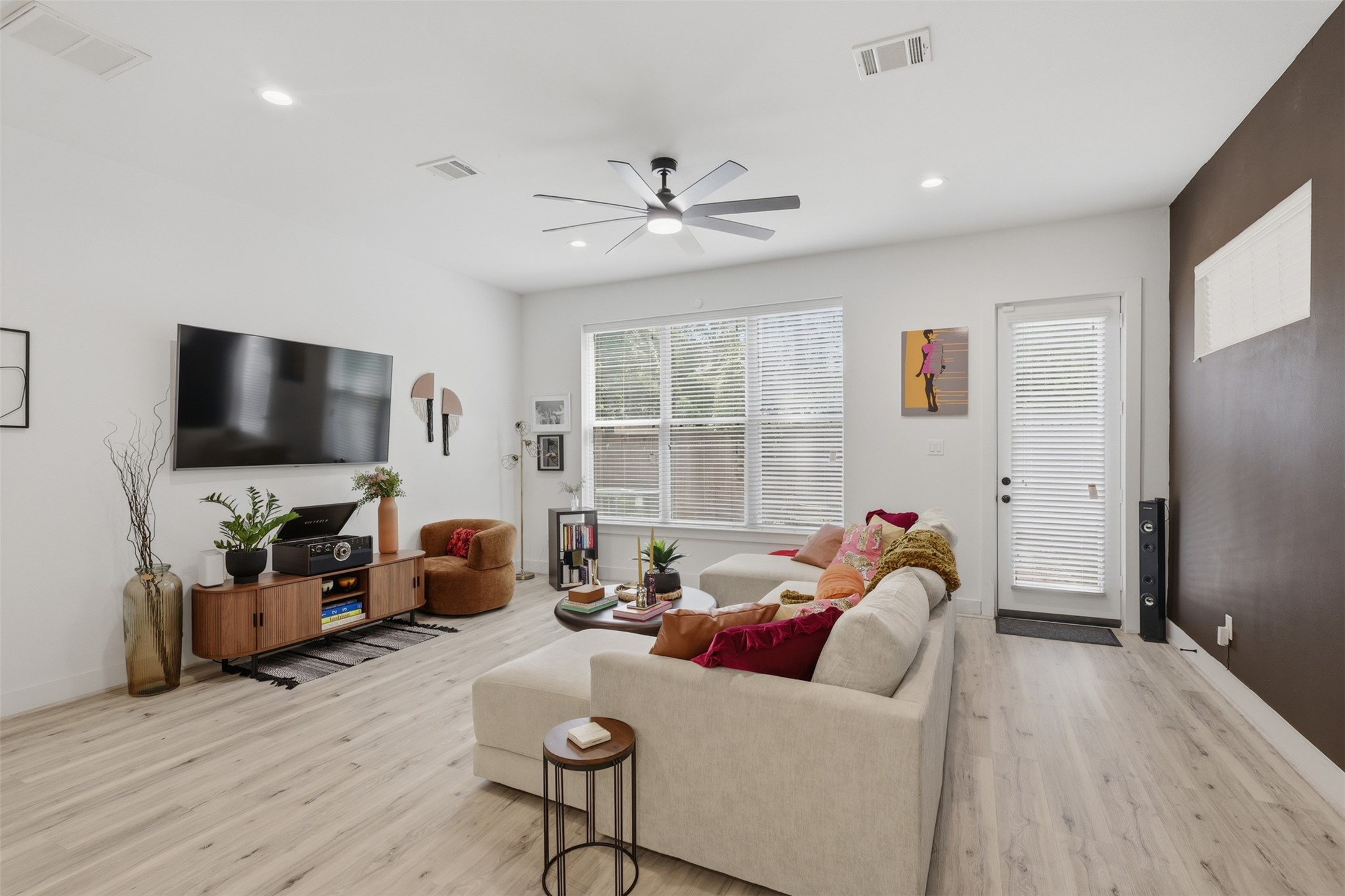 6833 Paris Street Houston, TX 77021 - Photo 5 of 23 This inviting living room features modern decor with a spacious layout. It includes a large wall-mounted TV, stylish furniture, and ample natural light from a big window and glass door, creating a bright and cozy atmosphere.