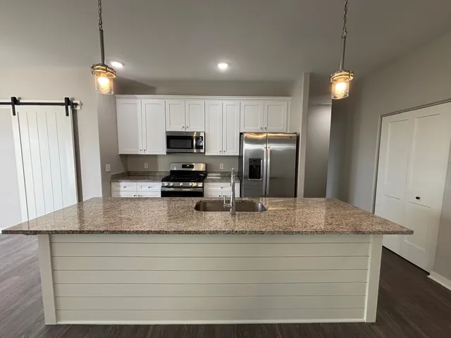 a kitchen with kitchen island granite countertop stainless steel appliances a refrigerator a stove a sink and cabinets