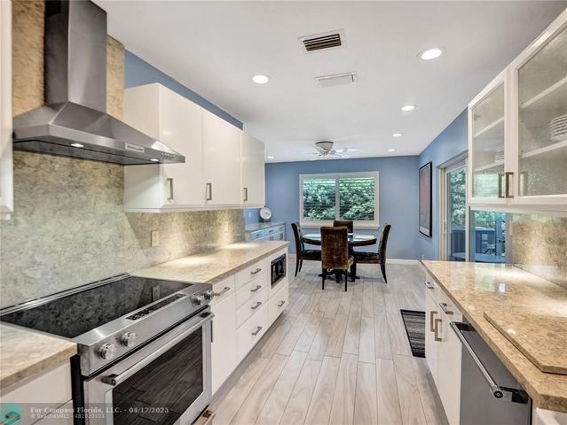 a kitchen with stainless steel appliances granite countertop a stove top oven a sink dishwasher and white cabinets with wooden floor