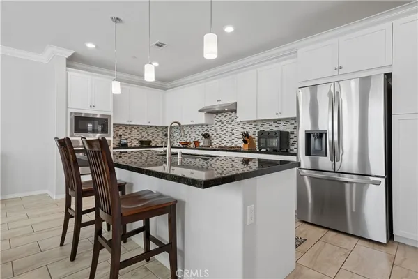 a kitchen with stainless steel appliances granite countertop a dining table chairs refrigerator and microwave