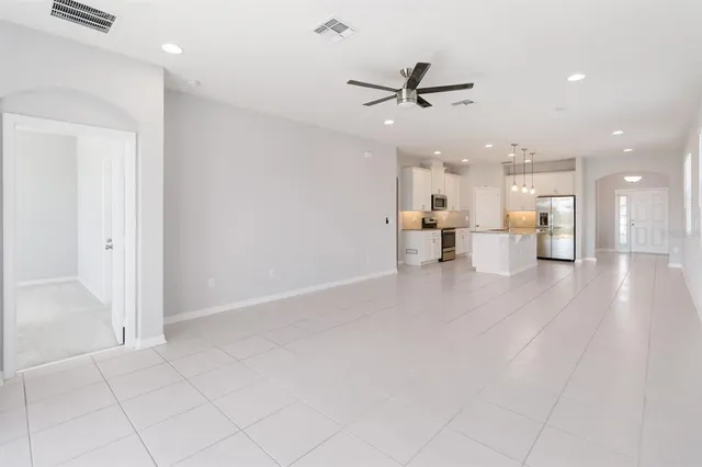 an empty room with wooden floor a ceiling fan and kitchen view