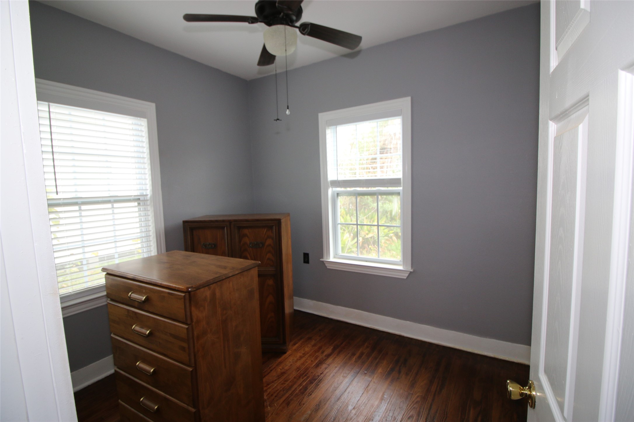 418 3rd Street Humble, TX 77338 - Photo 11 of 20 Discover the charm of the second bedroom, featuring elegant hardwood floors, soothing gray walls, and abundant natural light streaming through two large windows, creating a cozy and inviting retreat.