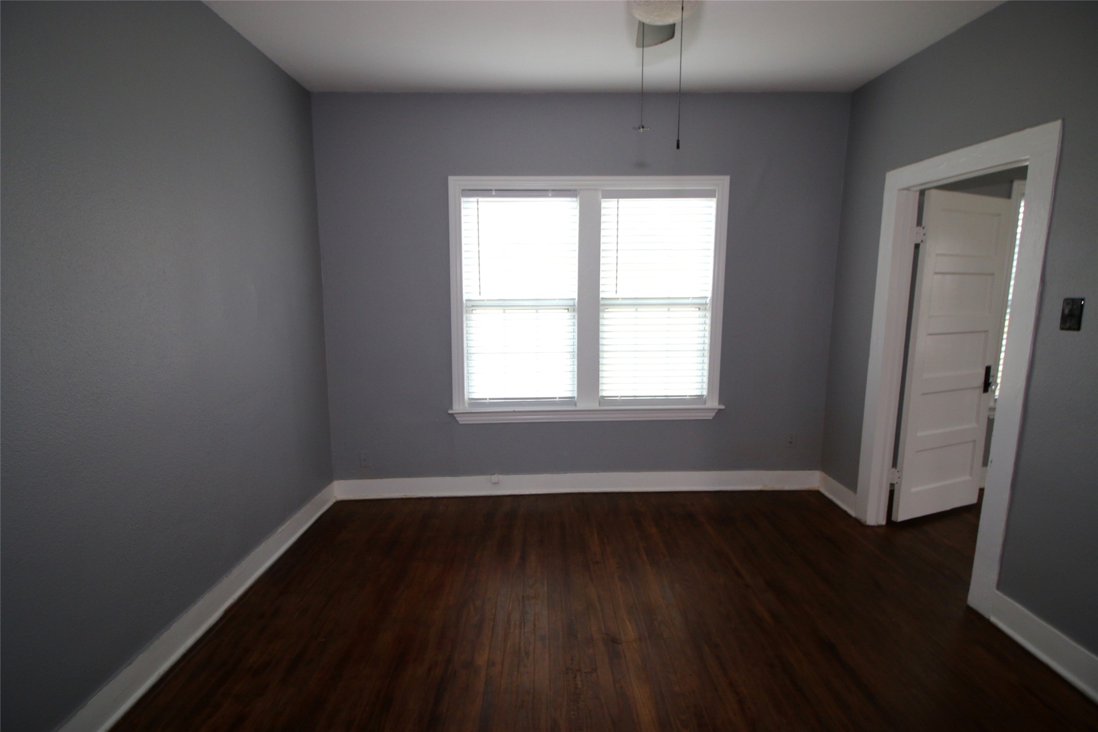 418 3rd Street Humble, TX 77338 - Photo 8 of 20 Discover serenity in this inviting primary bedroom, featuring rich hardwood floors, soothing gray walls, and abundant natural light through large windows.