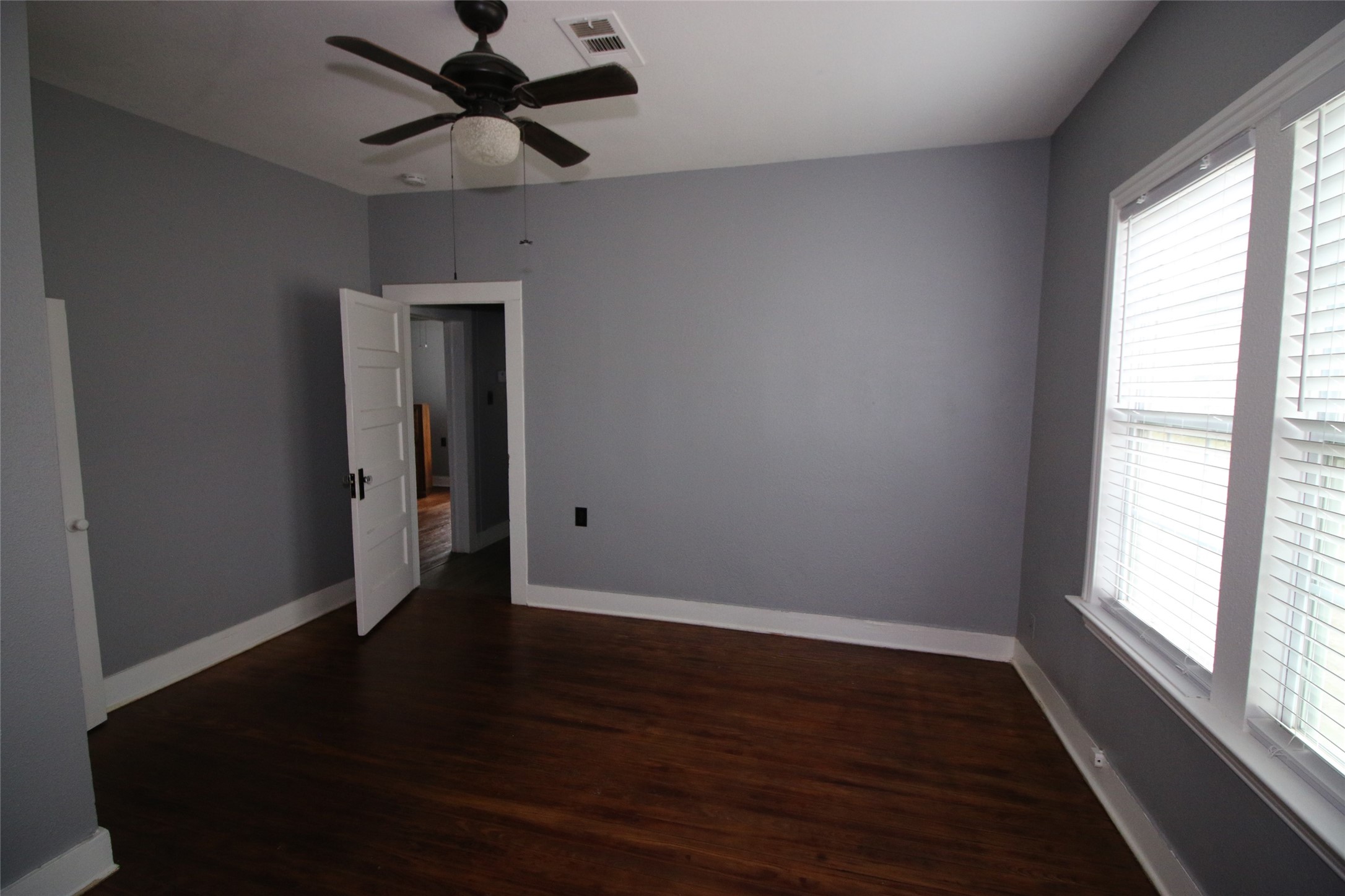 418 3rd Street Humble, TX 77338 - Photo 9 of 20 Discover the inviting charm of this primary bedroom, featuring rich hardwood floors, soft gray walls, abundant natural light from large windows, and a stylish ceiling fan for ultimate comfort.