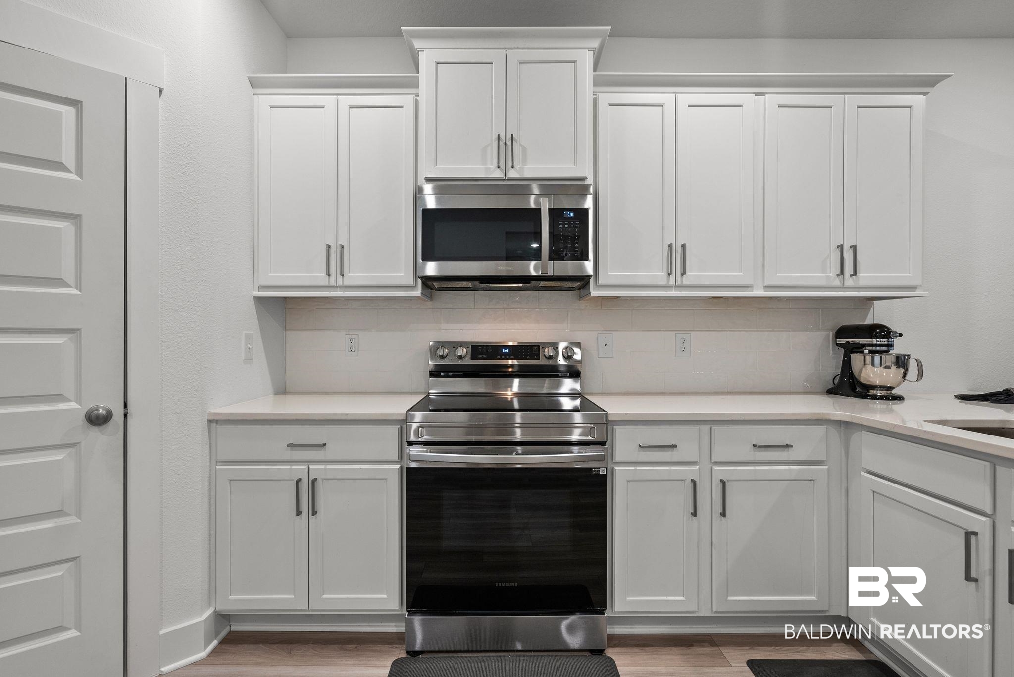9899 Willet Way Foley, AL 36535 - Photo 14 of 37 Contemporary kitchen featuring white cabinetry, stainless steel appliances, a tile backsplash, light-toned countertops, and wood-finish flooring