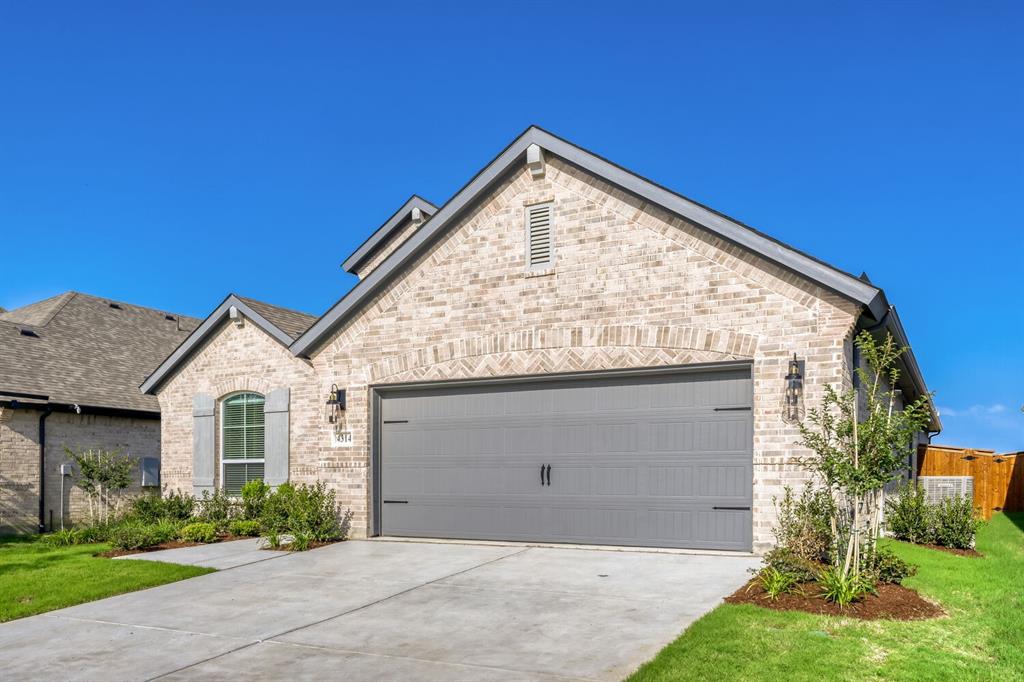 4314 Haley Way Oak Point, TX 75068 - Photo 27 of 28 Light-colored brick exterior featuring a grey garage door, concrete driveway, arched window with decorative shutters, and exterior wall sconces