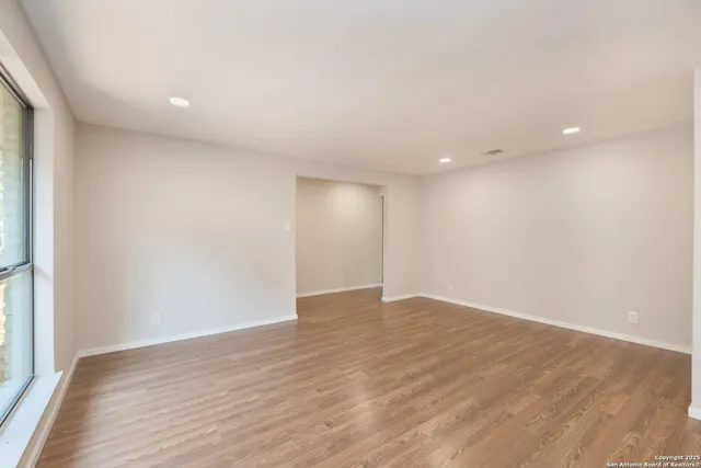 a view of an empty room with wooden floor and a window