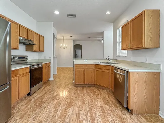 a view of an empty room with wooden floor and a kitchen