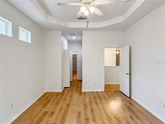 an empty room with wooden floor chandelier fan and windows